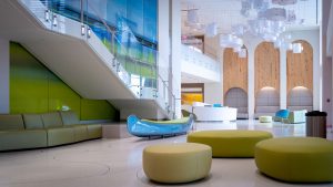 Interior view of a lobby at Exterior view of the MUSC Shawn Jenkins Children’s Hospital and the Pearl Tourville Women’s Pavilion.  There is a canoe playfully designed in the white lobby with green furniture.
