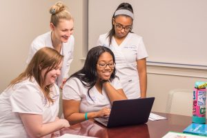 College of Nursing students happily gather around a computer.
